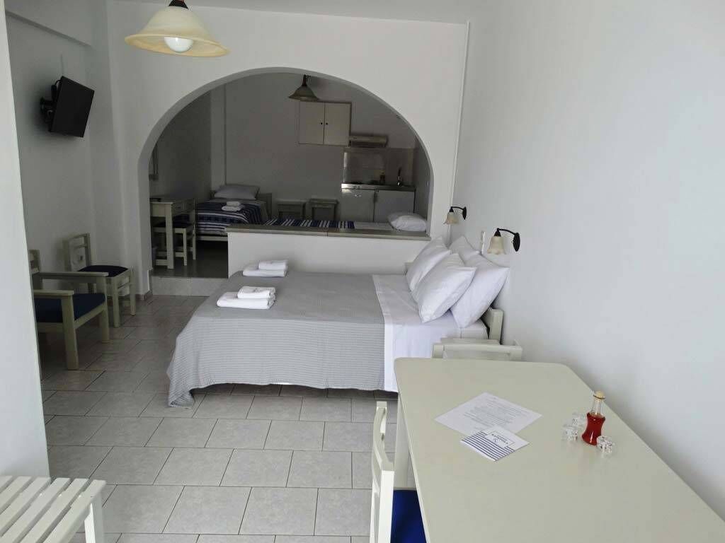 Ein Hotelzimmer mit Bett, Schreibtisch, Stuhl, Fernseher und einer sichtbaren Küchenzeile durch einen Bogen.