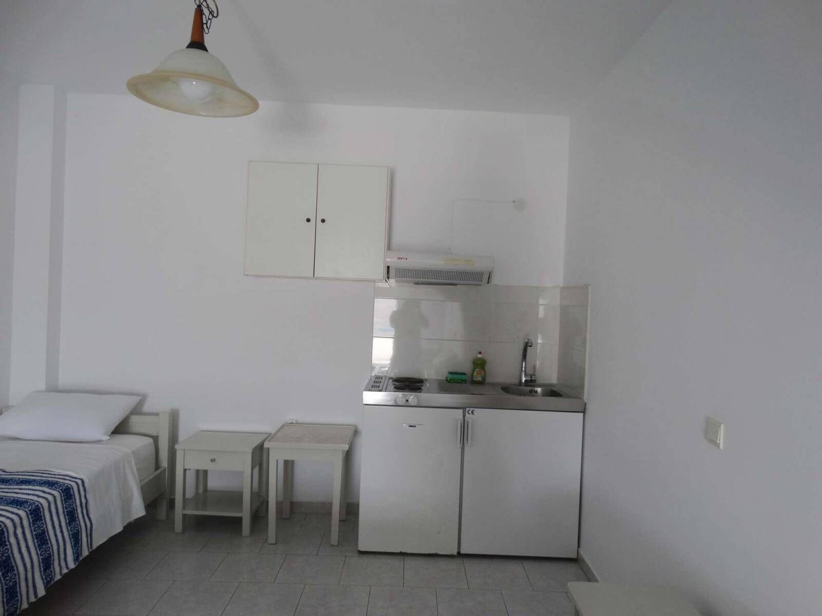 A compact room with a bed, a small table, a kitchenette with a refrigerator, and a cabinet.
