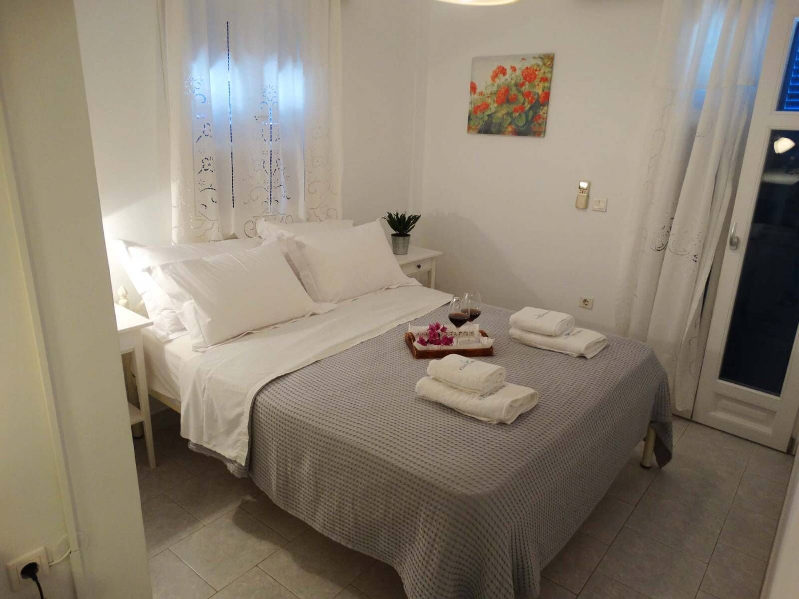 Una cama bien hecha con ropa de cama blanca, una mesita de noche con una planta y un cuadro en la pared.