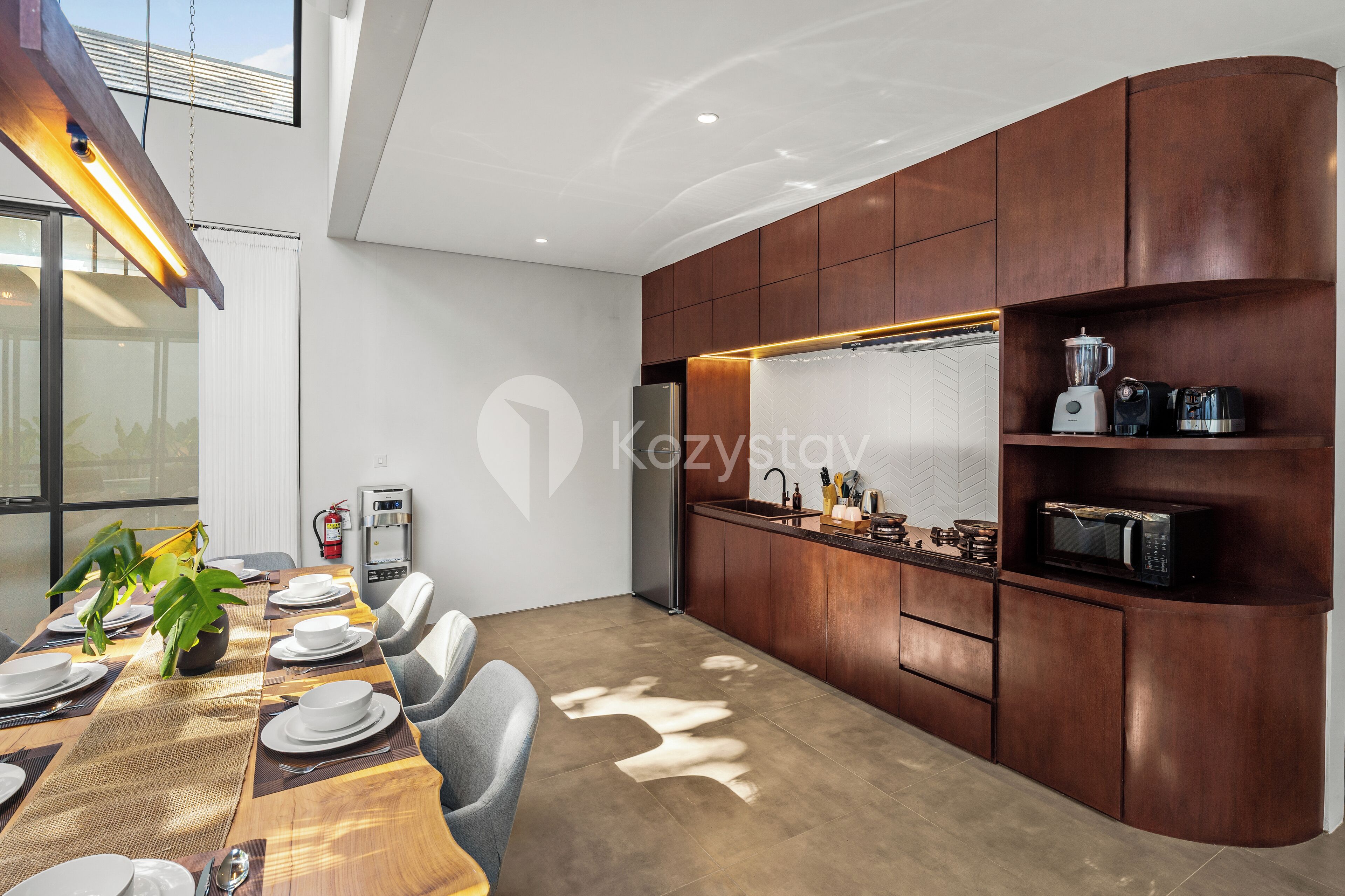 Une cuisine moderne dotée d’appareils électroménagers intégrés, un coin repas avec une longue table dressée pour le repas, et une vue sur l’extérieur.
