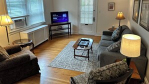 Un salon comprenant un canapé, un fauteuil, une table basse, un téléviseur et des lampes.