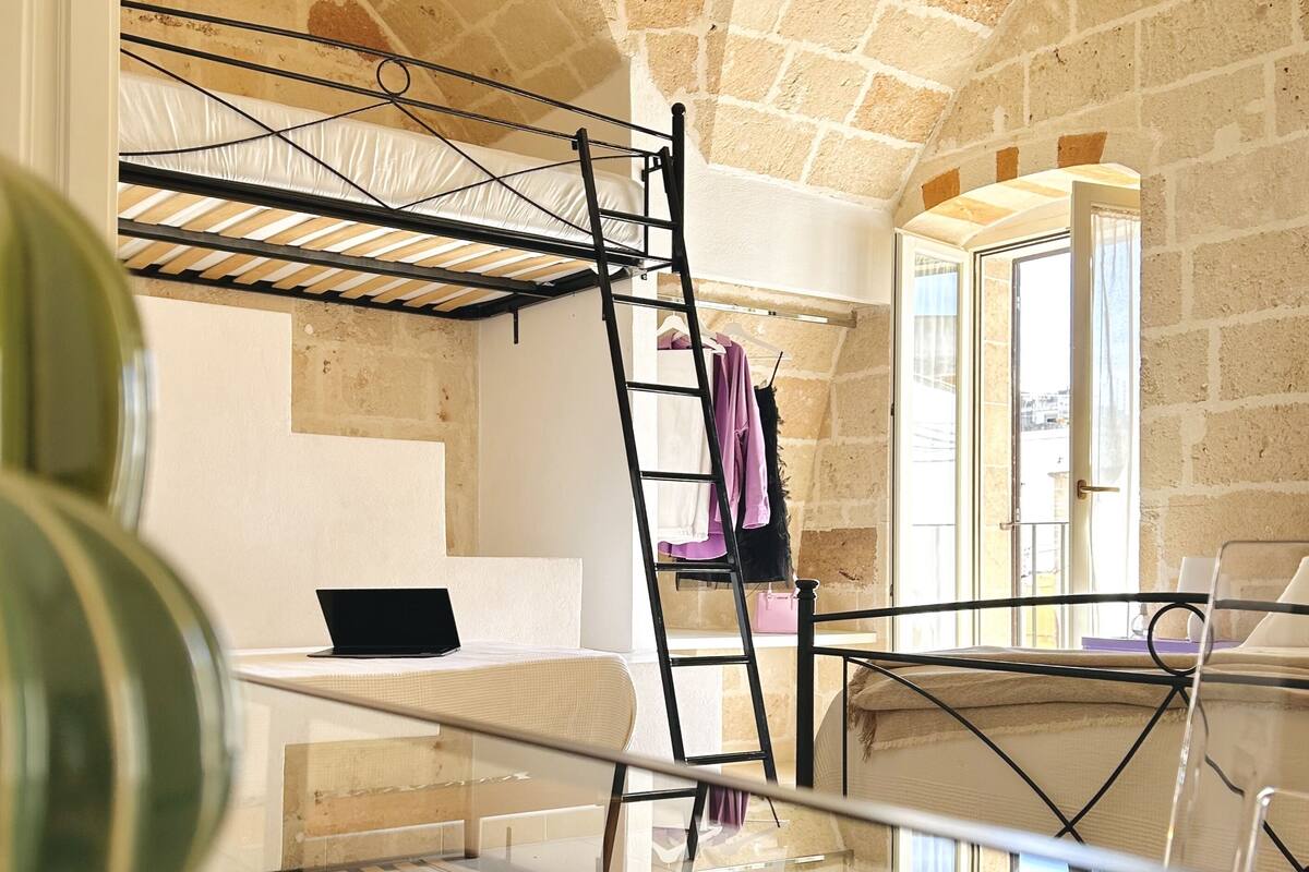 Une pièce avec un lit superposé, un ordinateur portable posé sur une petite table et une table en verre au premier plan.