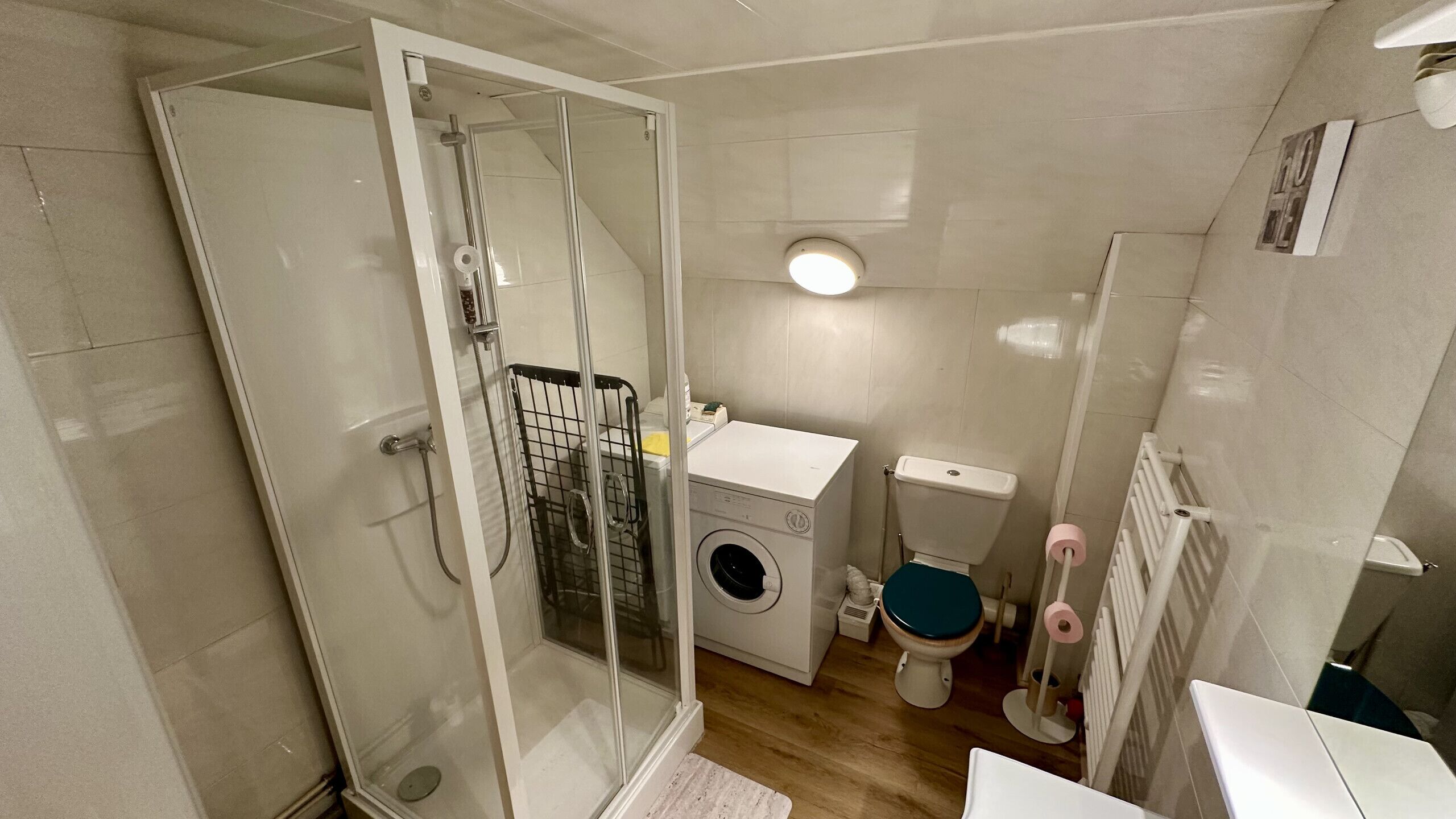 Een compacte badkamer met een douchecabine, een wasmachine, een toilet en een radiator.
