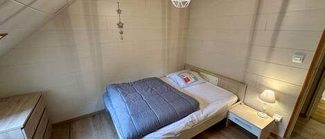 A small, single-bed room with a sloped ceiling, a bedside table with a lamp, and a wall-mounted star decoration.