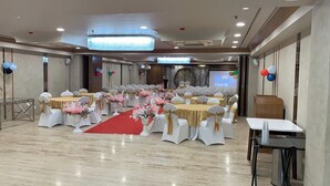 A banquet hall with round tables, white chairs, and red carpets. - Pam Inn Hotel Vadodara (Vadodara)