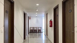A corridor with wooden doors numbered 2014 and 2015, a fire extinguisher on the wall, and a bench in the distance. - Pam Inn Hotel Vadodara (Vadodara)