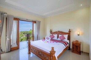 A spacious bedroom with a large bed, a wooden headboard, a nightstand, and a balcony with curtains. - Atuh Galaxy Cottage (Penida Island)