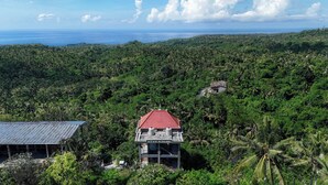 Un edificio de dos pisos con techo rojo, rodeado de exuberante vegetación tropical y vistas al océano.