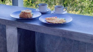 Una mesa con dos platos de comida y dos tazas, con vistas a un paisaje verde exuberante y el mar.
