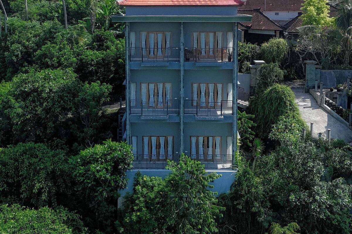 Un immeuble à plusieurs étages doté de balcons, entouré d’une végétation luxuriante et surplombant un ciel dégagé.