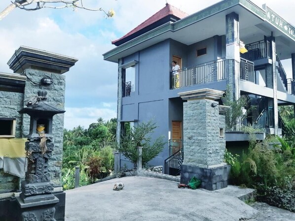 A two-story building with a balcony on the upper floor, stone pillars, and a clear sky. - Atuh Galaxy Cottage (Penida Island)