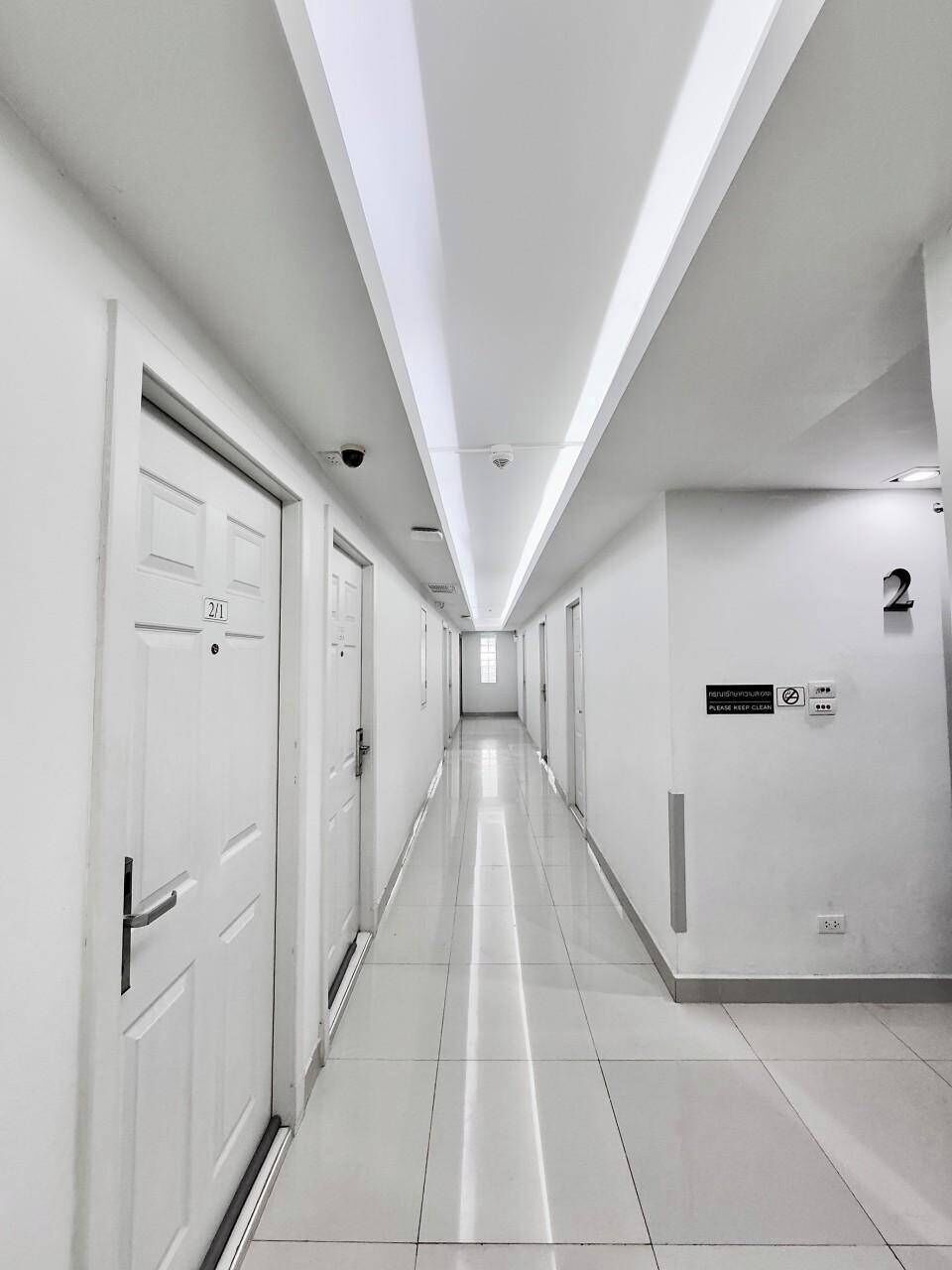 Um corredor comprido e estreito com portas brancas, cada uma delas identificada por um número.