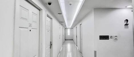 Um corredor comprido e estreito com portas brancas, cada uma delas identificada por um número.
