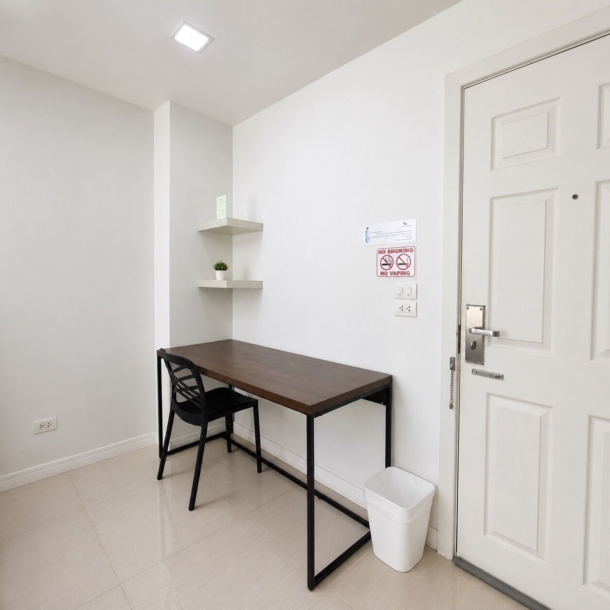 Habitació petita i neta amb escriptori, cadira i una porta blanca.