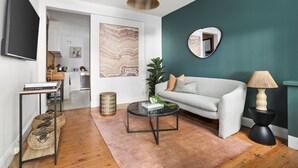A modern living room with a grey sofa, a round coffee table, a TV, and a mirror on the wall.