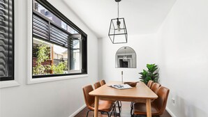 A dining area with a wooden table and leather chairs, a hanging light fixture, and a view of the outside through a large window.