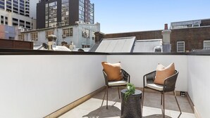A rooftop terrace with two chairs and a small table, surrounded by city buildings.