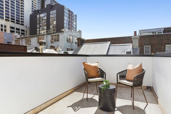 A rooftop terrace with two chairs and a small table, surrounded by city buildings.