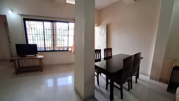Um quarto espaçoso com uma mesa de jantar e cadeiras, uma televisão em um suporte, e uma janela com grades de metal.
