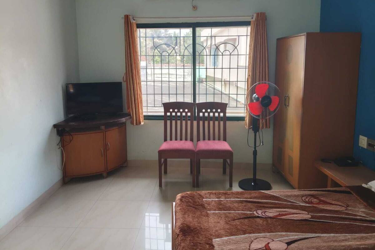 Una stanza con un letto, una televisione, un armadio, una sedia e una ventola da terra.