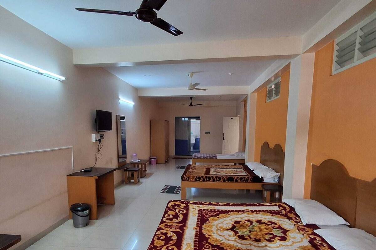 Una camera d'albergo con due letti singoli, una scrivania, una sedia, un televisore e una ventola a soffitto.