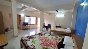 Quarto de hotel com uma cama grande, uma escrivaninha, uma cadeira e um espaço de refeições com mesa e cadeiras.