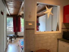 Une pièce chaleureuse avec un plafond en bois, une fenêtre décorée d’une étoile, un petit sapin de Noël et un meuble rouge.