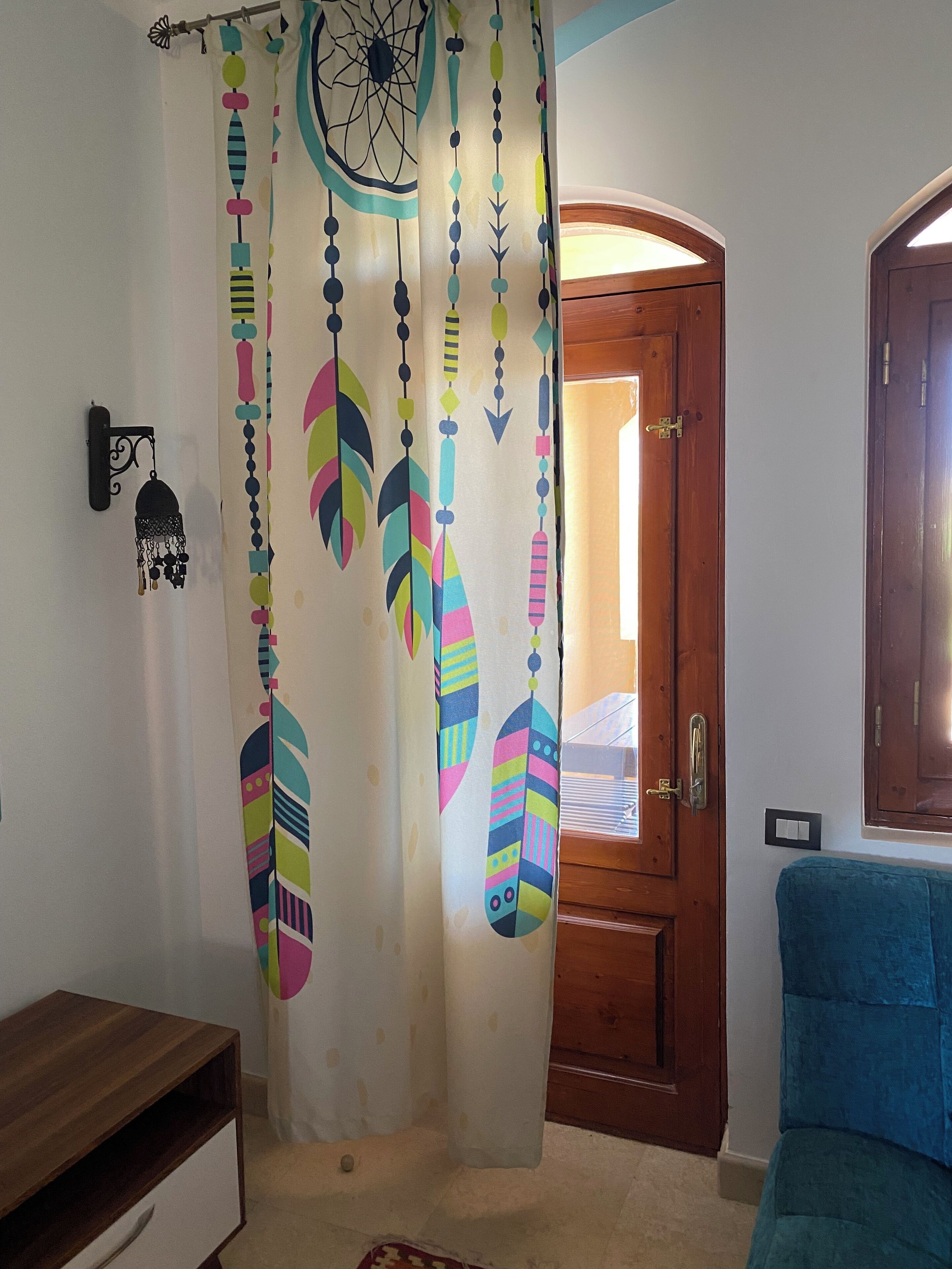 Une pièce avec une porte en bois, un canapé bleu et un rideau orné de motifs colorés en forme de plumes.