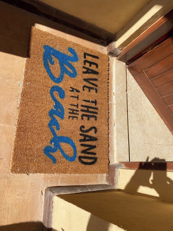 Een deurmat met de tekst 'LEAVE THE SAND AT THE Beach' en een blauw golfpatroon.