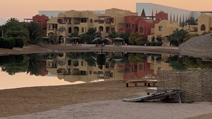 Ein Hotel mit mehreren Gebäuden, einem Spiegelbild im Wasser und einem sandigen Vordergrund.