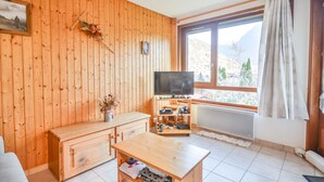 Una habitación acogedora con paredes de madera, un televisor, un aparador de madera y una ventana con vistas a montañas.