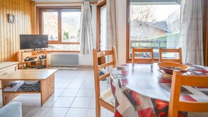 Una habitación acogedora con detalles de madera, televisión, una mesa de comedor con sillas y ventanas amplias con vistas al exterior.