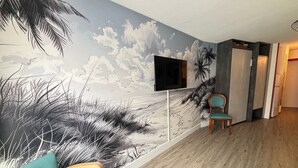 Quarto com um mural de praia, uma televisão de tela plana na parede e duas cadeiras azul-turquesa.