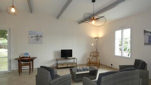 A spacious living room with grey wicker furniture, a television, and a ceiling fan. - Vendée House 3 BR, Pet-Friendly, Near Beach (Notre-Dame-de-Monts)