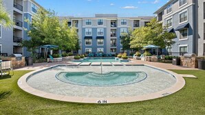 A modern apartment building with a central swimming pool, surrounded by well-maintained lawns and trees. - Charming 1-bedroom Haven I Frisco Dallas I Pool / Gym / Work Space (Frisco)