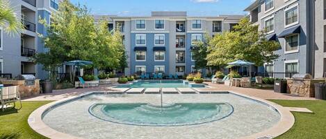Un immeuble d’appartements moderne doté d’une piscine centrale, entouré de pelouses et d’arbres bien entretenus.