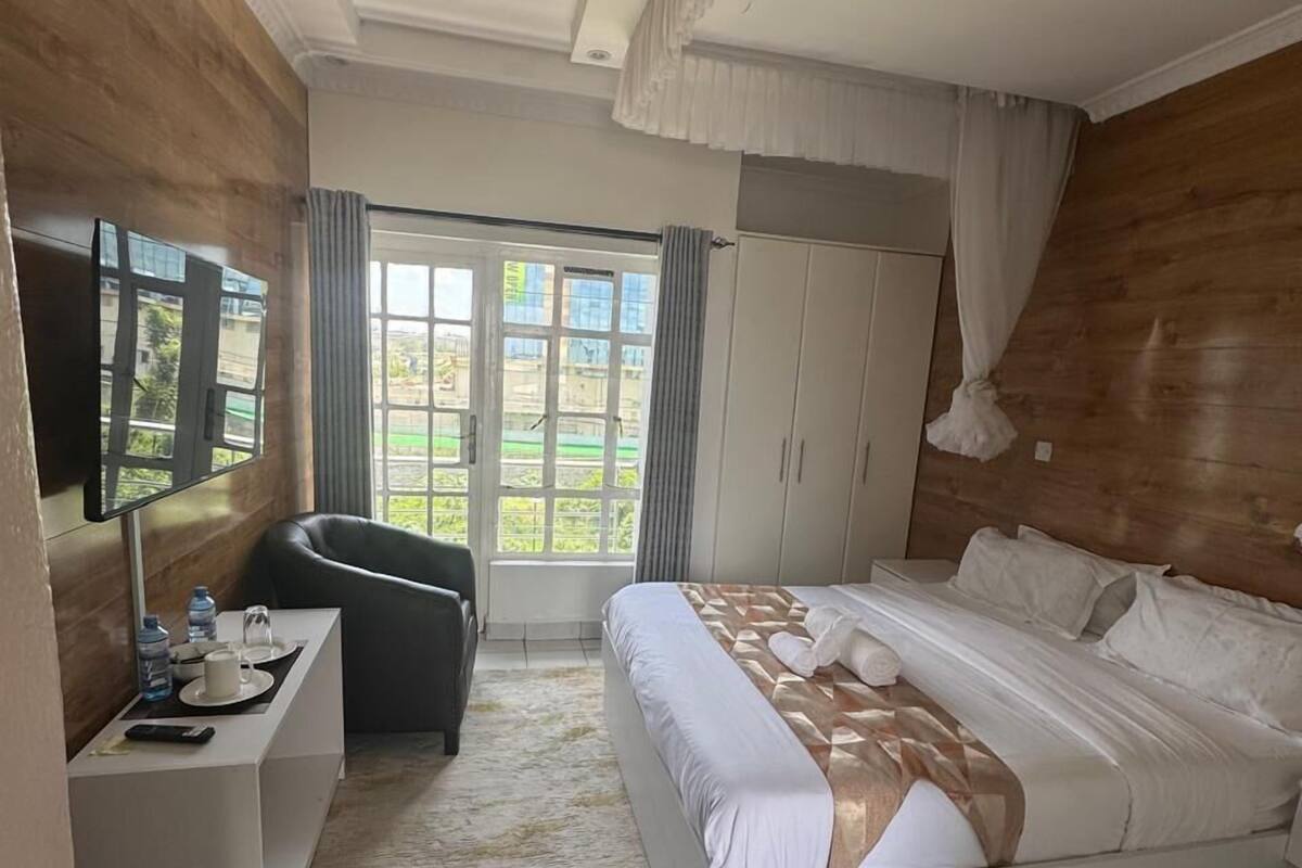 A hotel room with a bed, a desk with a chair, a television, and a view of the outdoors through a large window.