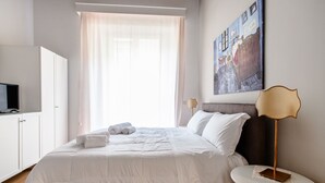 A neatly made bed with white linens, a bedside table with a lamp, and a painting on the wall.