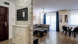 Ένα μοντέρνο σαλόνι με έναν καναπέ, ένα τραπέζι τραπεζαρίας με καρέκλες, έναν διακοσμητικό τοίχο με έναν καθρέφτη και ένα ξύλινο δάπεδο.