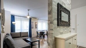 Ένα μοντέρνο σαλόνι με έναν καναπέ, ένα τραπέζι φαγητού και μια κουζίνα με διακοσμητικό τοίχο και έναν καθρέφτη.