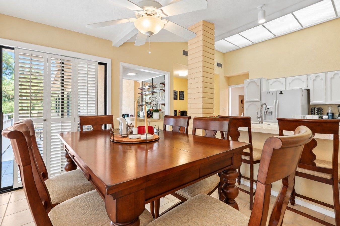 A dining room with a large wooden table, six chairs, and a ceiling fan.