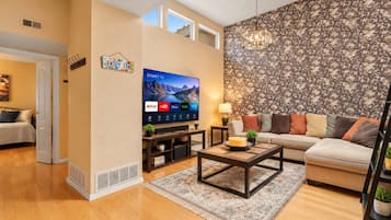A living room with a flat-screen TV, a sofa, a coffee table, and a patterned wallpaper.