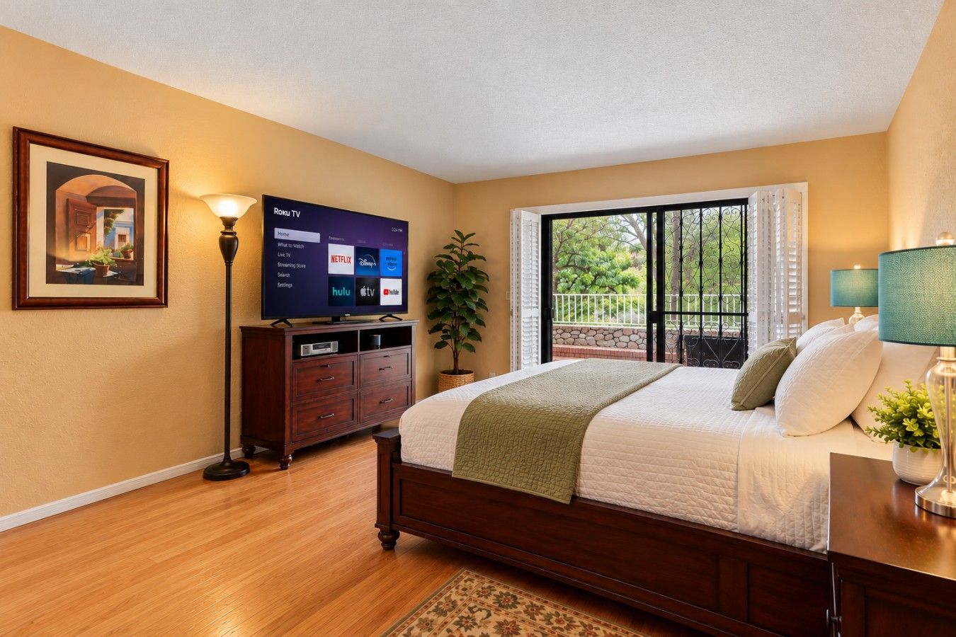 A bedroom with a bed, a TV, a dresser, and a window with a view.