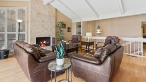 Ein Wohnzimmer mit Ledersofas, einem Kamin, einem Essbereich und einer Treppe.