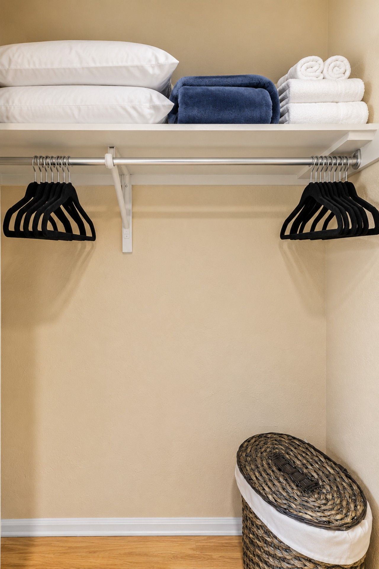 A closet with hanging space, a shelf with folded towels, and a basket on the floor.