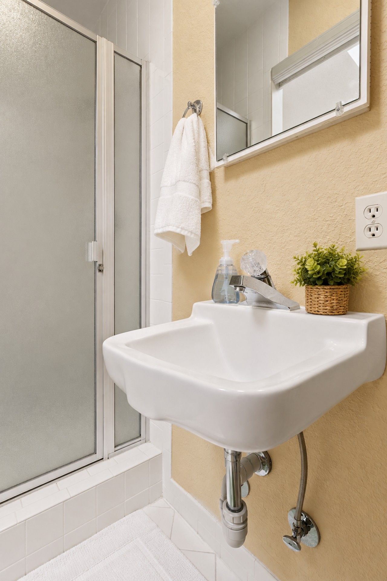 A bathroom with a white sink, a glass shower enclosure, a towel hanging on the wall, and a small potted plant.