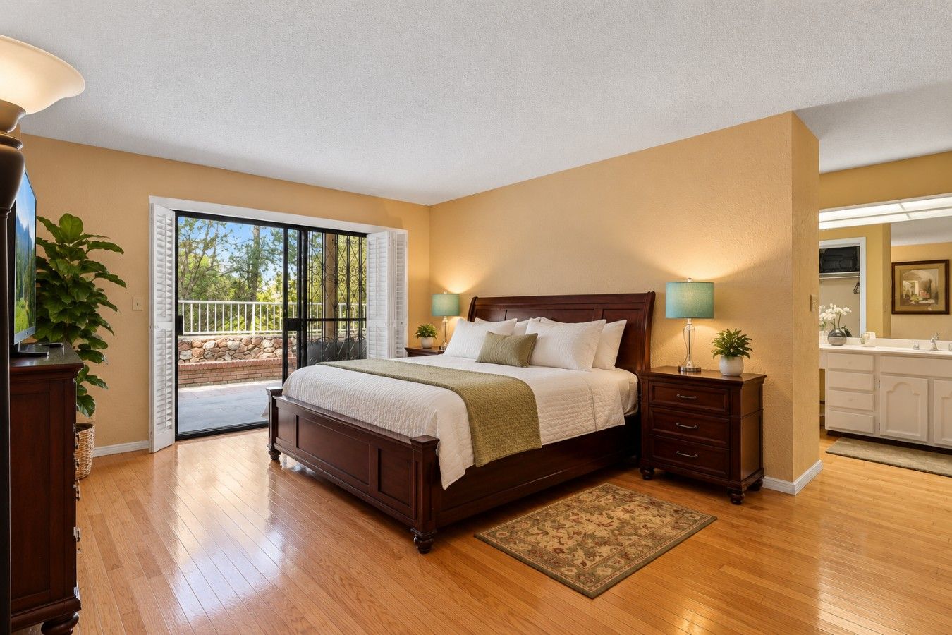 A bedroom with a large bed, a nightstand, a dresser, a sliding glass door to a balcony, and a view of the outdoors.