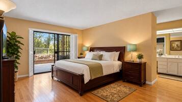 A bedroom with a large bed, a nightstand, a dresser, a sliding glass door to a balcony, and a view of the outdoors.