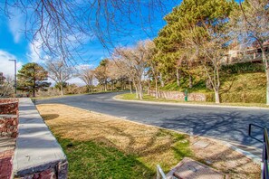 Una calle residencial con una curva, árboles, un muro de piedra y una acera.