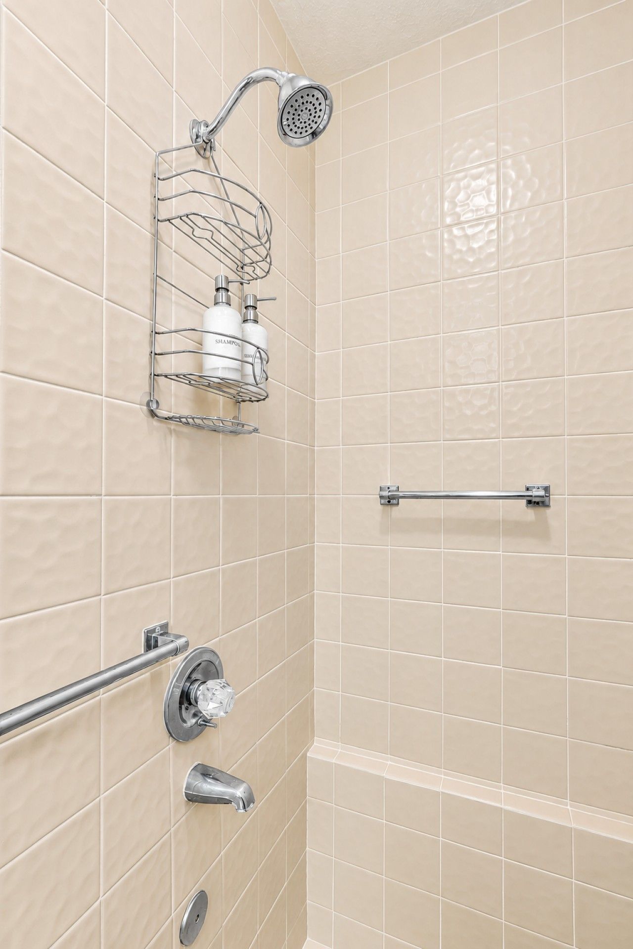 Un bagno con piastrelle color crema, una doccia con soffione estraibile, un portasciugamani e una barra di sostegno.